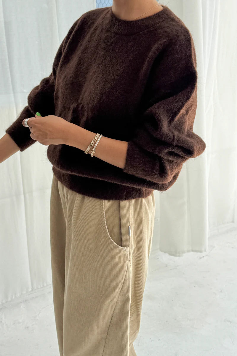 Person wearing a brown sweater and beige pants against a white background